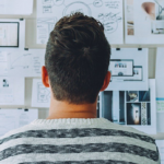 Professionista che osserva progetti e documenti di lavoro su parete con schizzi e planimetrie