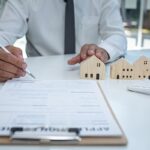 Architetto con casco esamina modellini di case su documenti contrattuali immobiliari