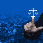 Mano che tocca simbolo della bilancia della giustizia su sfondo città digitale blu, rappresenta legal tech e innovazion…