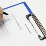 Mano che firma documento legale con penna su clipboard blu