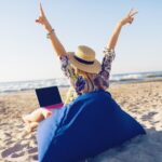 Donna lavora da remoto con laptop in spiaggia tropicale, smart working e telelavoro