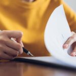 Persona che firma documento legale con penna, rappresentazione di sottoscrizione contrattuale e competenza giurisdizion…