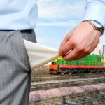 Mano di professionista che tiene documenti con treno e impianto industriale sullo sfondo, simbolo di transazioni patrim…