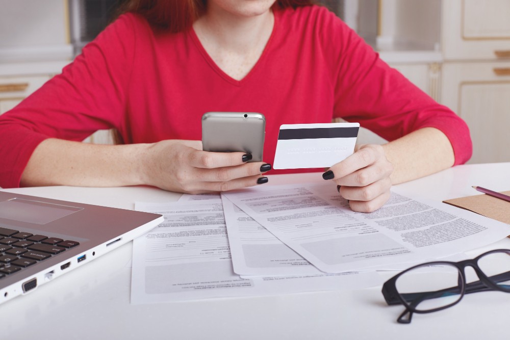 il-modello-femminile-irriconoscibile-in-maglione-rosso-si-siede-al-tavolo-di-lavoro-circondato-da-documenti-e-computer-portatile