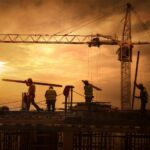 Cantiere edile con operai al tramonto, simbolo della sicurezza e della normativa nel settore costruzioni