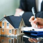 Modello di casa con documenti legali e firma su contratto di locazione immobiliare
