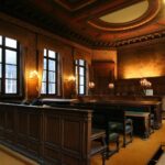 Aula di tribunale con banchi in legno scuro, illuminazione calda e arredamento solenne per procedimenti legali