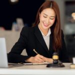Avvocato donna in studio legale al lavoro su documenti con laptop e statua della giustizia