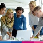 Gruppo di professionisti diversi riuniti attorno a laptop in riunione di lavoro collaborativa
