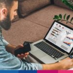 Uomo analizza fatture e dati fiscali su laptop con grafici e documenti di e-commerce