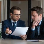 Due consulenti aziendali discutono di documenti fiscali in ufficio moderno