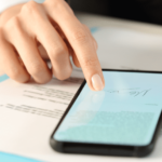 Mano su smartphone con documento fiscale e fogli di lavoro contabili