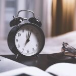 Sveglia nera su scrivania di lavoro con laptop e documenti, simbolo di urgenza e scadenze professionali