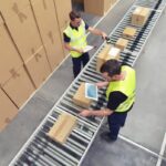 Lavoratori in magazzino su nastro trasportatore durante controllo documentazione e comunicazioni amministrative
