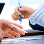 Professionista redige documento legale con penna mentre cliente esamina contratto
