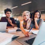 Giovani professionisti in riunione di lavoro collaborativo con laptop e documenti in ufficio moderno
