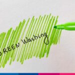 Mano che evidenzia con pennarello verde la scritta "Green Washing" su carta bianca, simbolo della pratica ingannevole d…