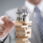 Mano che costruisce torre di legno con casa modello - stabilità immobiliare e diritto