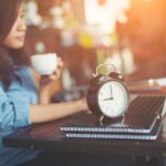 Sveglia su scrivania con laptop in ufficio, simbolo di orario di lavoro e accordi contrattuali del lavoratore subordina…